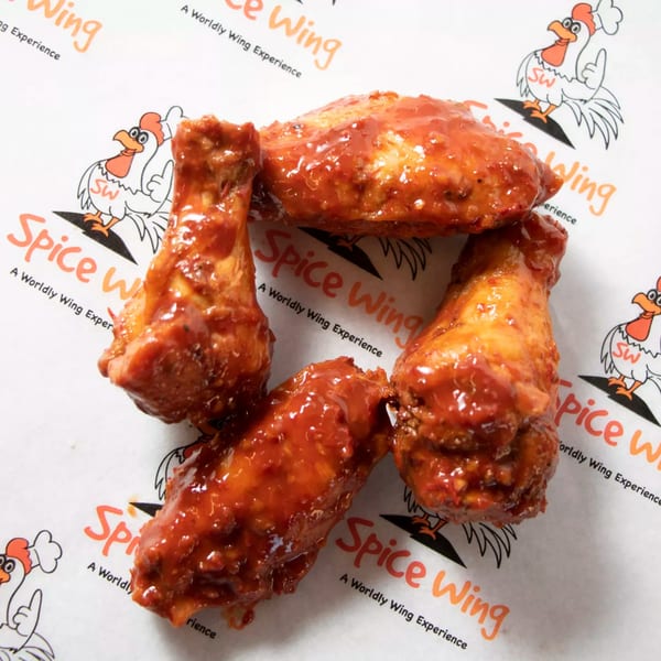 Four glistening Spice Wing chicken wings, coated in a rich red sauce, arranged on branded paper.