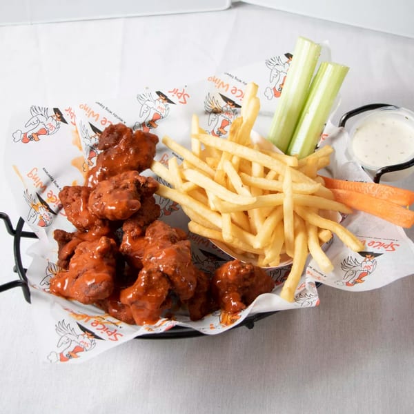 Spice Wing's saucy chicken wings, golden fries, celery, carrots, and ranch dressing in a basket.