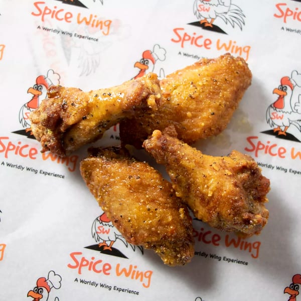 Four golden-brown Spice Wing chicken wings, seasoned with pepper, resting on branded white paper.