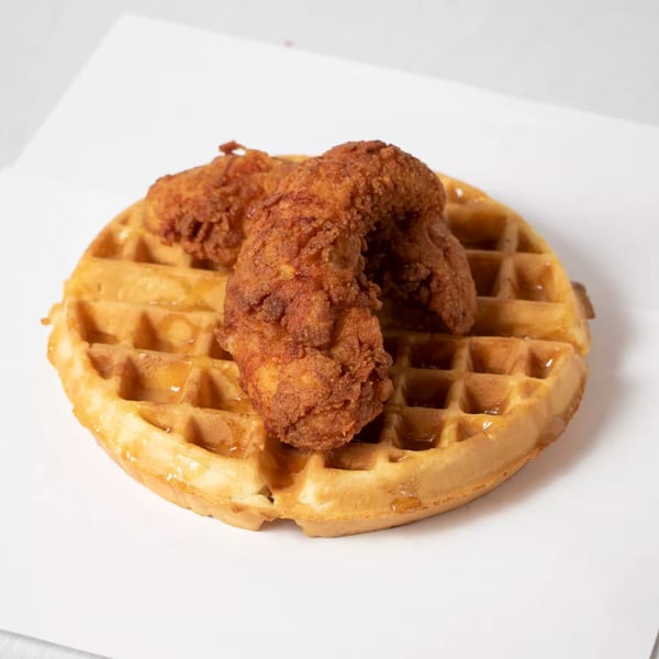 Golden-brown fried chicken tenders on a waffle drizzled with syrup, a classic Spice Wing dish.