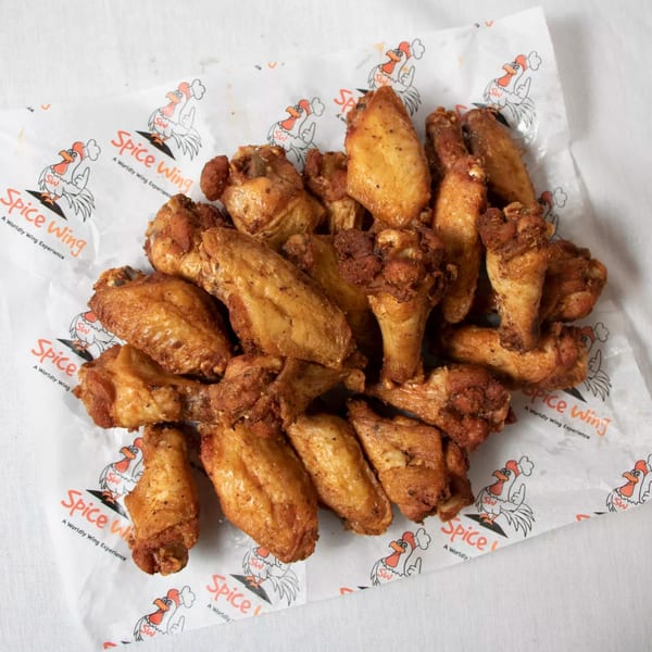 Spice Wing's crispy chicken wings, seasoned and golden brown, served on branded wax paper.
